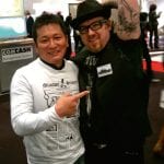 Hirokazu Mizutani zeigt auf einen Mizutani Fan mit einem Armtattoo auf einer Messe